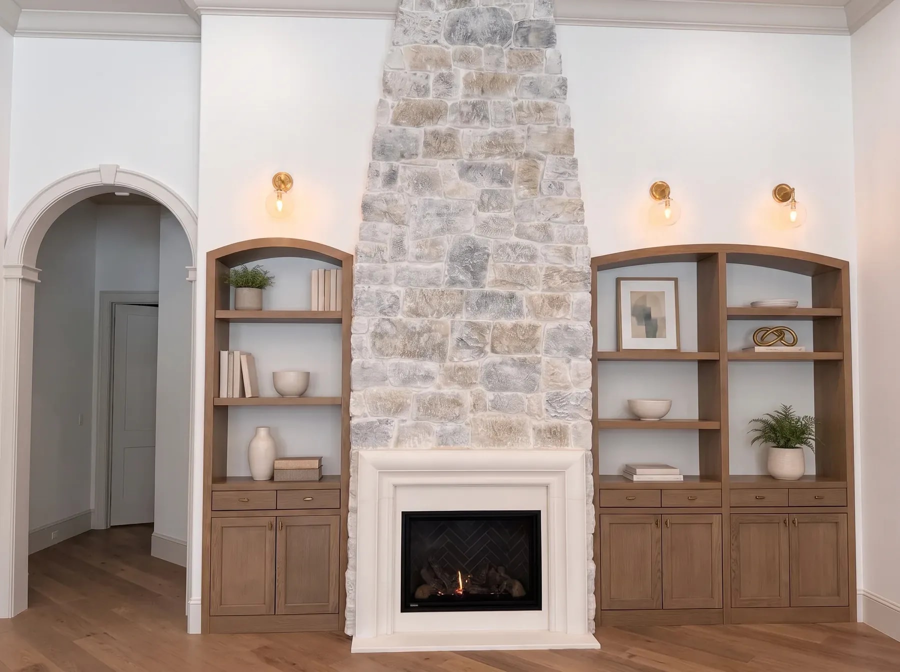 Cast stone fireplace with a full-height stone chimney, arched white oak built-ins and brass sconces