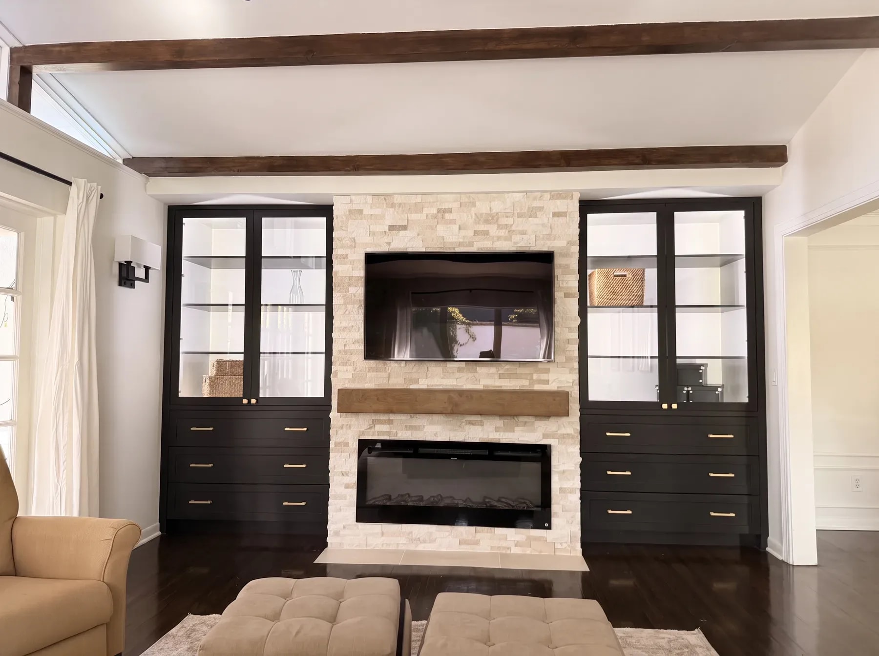 Light stacked stone television wall with a timber mantel beam, linear fireplace and black glass-front cabinetry