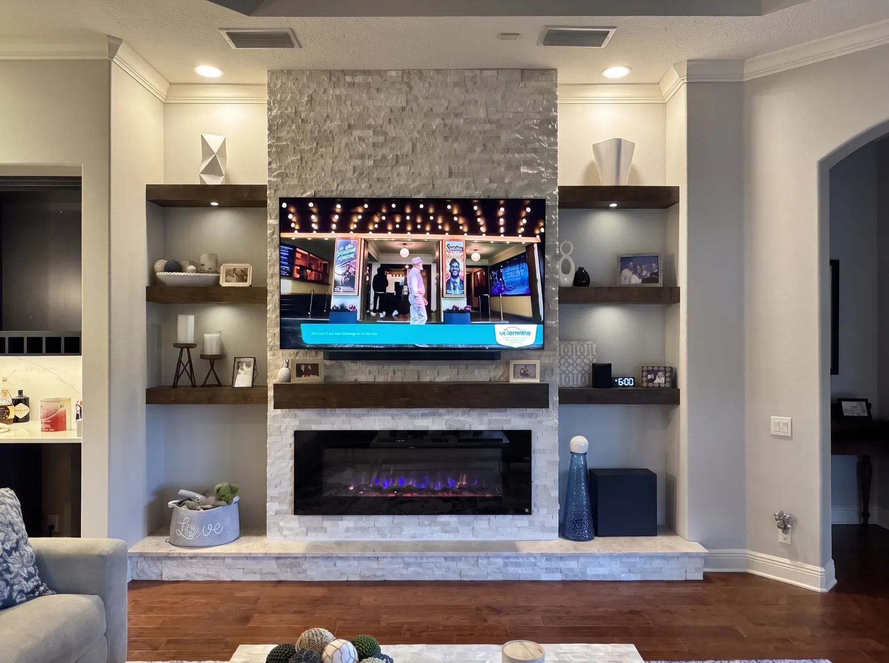 Light stacked stone column with floating walnut shelves, a timber mantel and a linear fireplace above a stone hearth