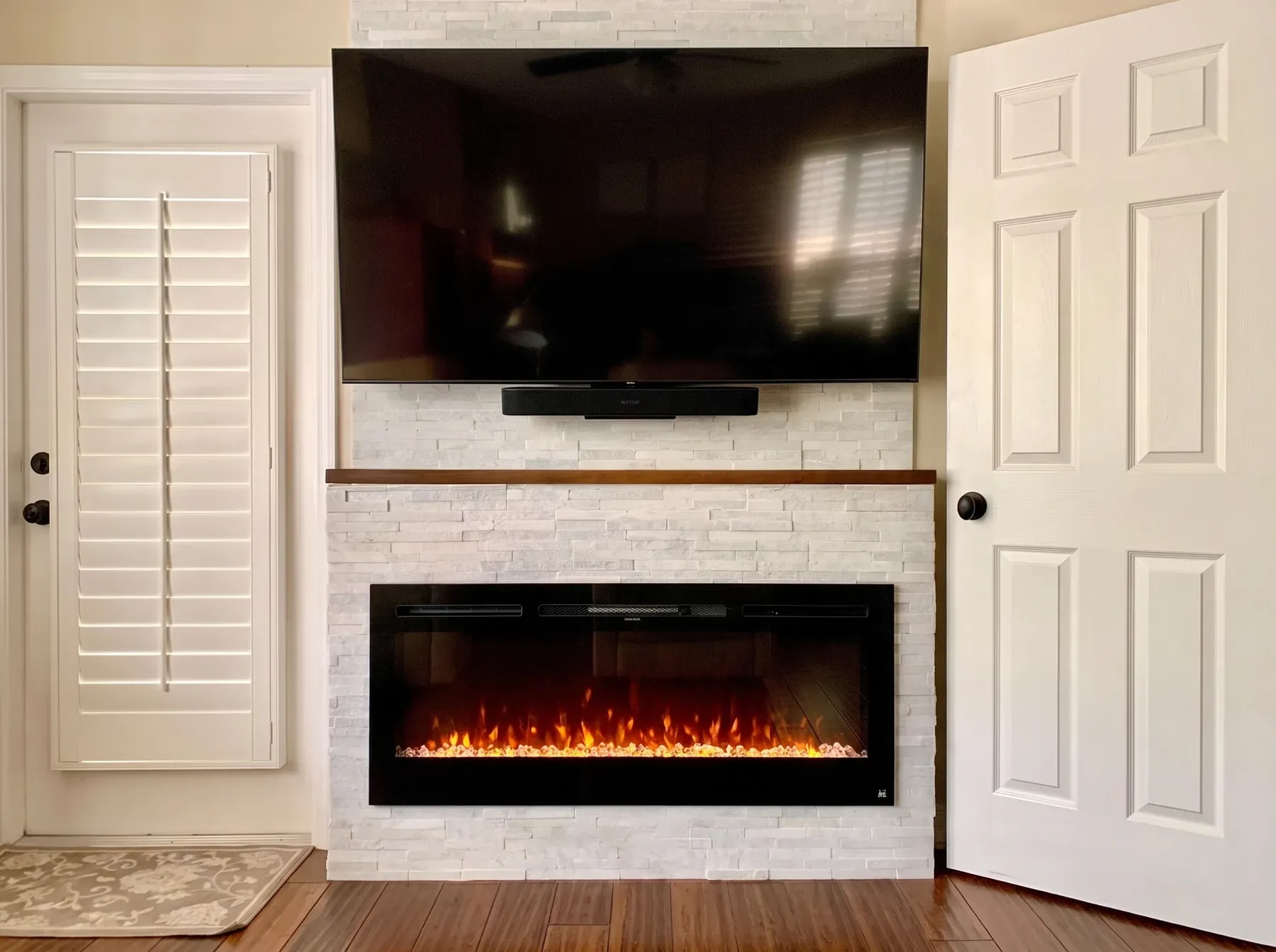 White stacked stone wall with a walnut mantel shelf, linear fireplace and wall-mounted television